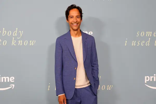 Danny Pudi wearing a navy blazer with peach top