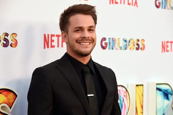 Johnny Simmons wearing a black suit, smiling