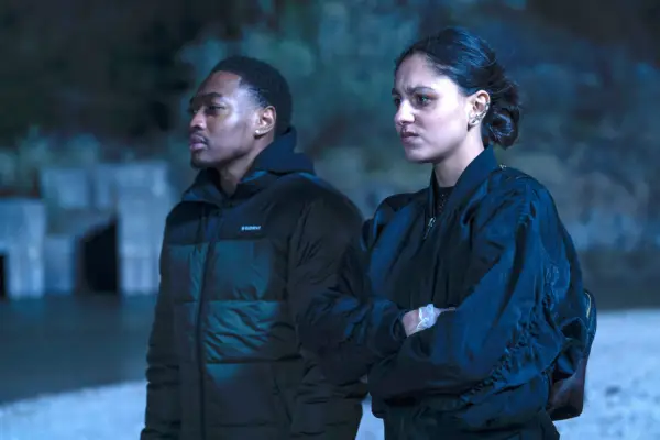 Ben and Rani in a remote setting late at night, wearing dark coloured clothing with serious expressions on their face