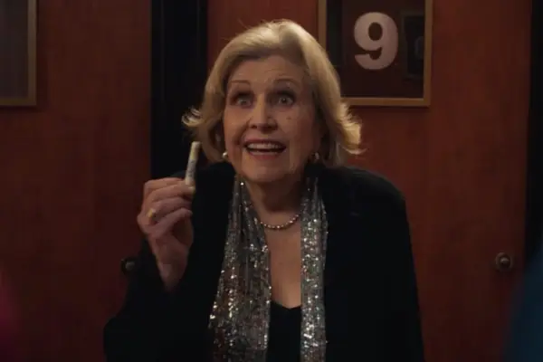 Anne Reid holds a rolled-up bank note in one hand and smiles enthusiastically