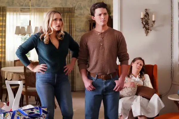 Emily Osment and Montana Jordan standing in a living room looking angry with Zoe Perry sitting on an armchair in the background.