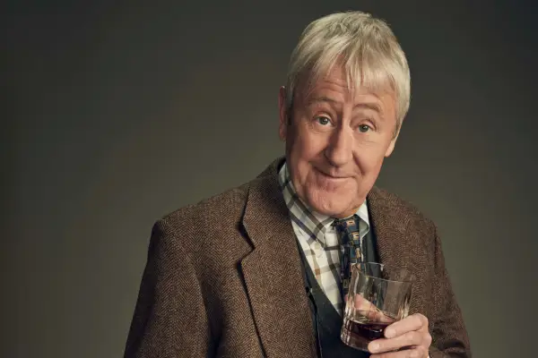 Nicholas Lyndhurst plays Dr Alan Cornwall, wearing a suit and holding a glass of whisky