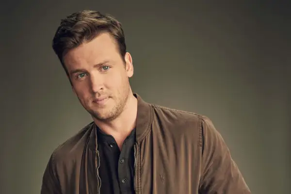 Jack Cutmore-Scott as Freddy Crane, wearing a brown jacket and black t-shirt