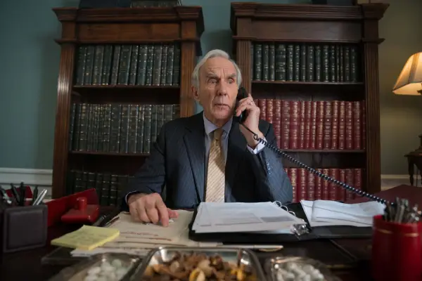 Charles answers the phone in his office, with shelves of fancy hardback books behind him