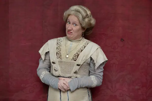 Martha Howe-Douglas as Lady Button in Ghosts, standing with her hands together and frowning at the camera