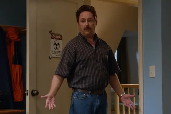 Scott Grimes as Matty Bennett wearing a shirt and jeans, stood in a bedroom doorway