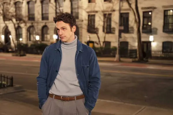 Sebastiano Pigazzi plays Giuseppe, standing in the street, wearing a grey polo neck, dark jacket and trousers, hands in pockets