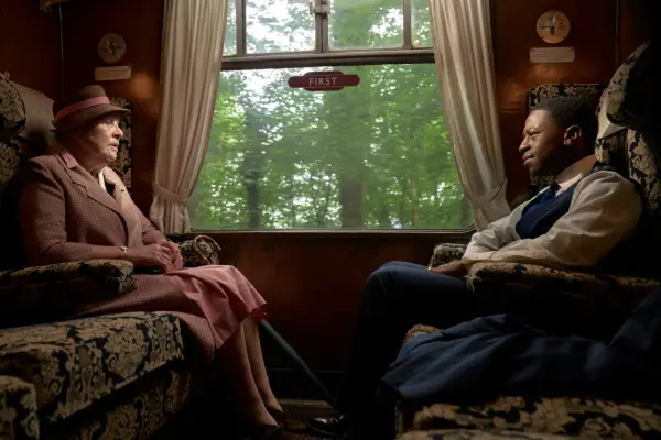 A man and a woman sit across from one another in an old-fashioned train carriage