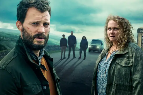 Jamie Dornan as Elliot and Danielle Macdonald as Helen looking concerned, with three other characters and a van in the background