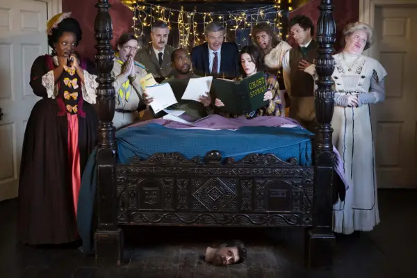 Ghosts season 5 cast Lolly Adefope, Jim Howick, Ben Willbond, Kiell Smith-Bynoe, Simon Farnaby, Charlotte Ritchie, Laurence Rickard, Mathew Baynton and Martha Howe-Douglas gathered around a wooden bed
