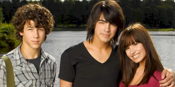 Nick Jonas standing next to Joe Jonas, who has an arm around Demi Lovato for Camp Rock