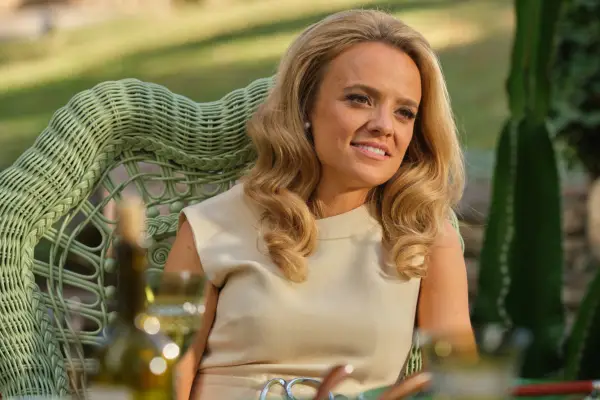 Laura Aikman as Dyan Cannon in Archie sitting on a garden chair wearing a dress.
