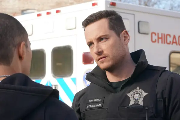 Jesse Lee Soffer as Jay Halstead in Chicago PD standing outside by an ambulance and wearing his police uniform, about to speak to someone.