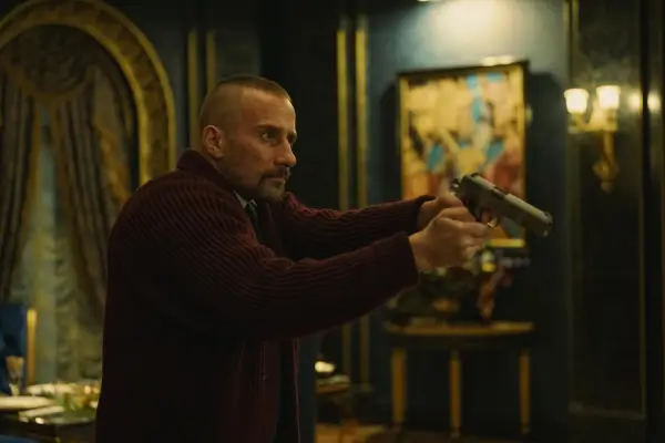 Matthias Schoenaerts in The Regime, holding a gun up at someone off screen