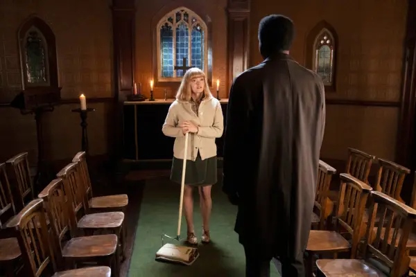 Natalie Quarry as Rosalind standing while holding a carpet cleaner while Zephryn Taitte as Cyril stands before her