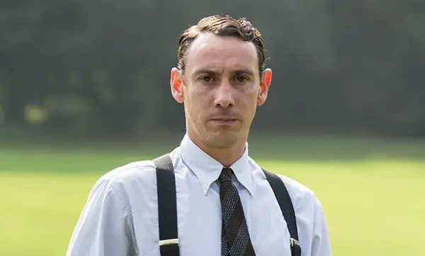 Al Weaver as Leonard Finch in Grantchester. He is stood in a field, wearing a white shirt and braces. He looks serious.