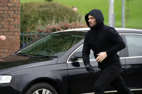 Charlie Cox as Michael Kinsella, wearing a hoodie with his hood up and walking by a car in Kin season 2