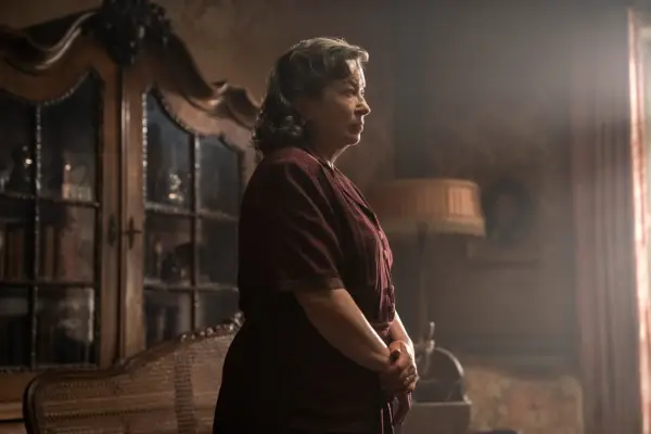 Marion Bailey as Madame Manec in All the Light We Cannot See wearing a red dress, with her hands by her waist