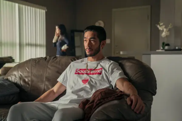 Justin Chien as Charles Sun in The Brothers Sun sitting on a brown sofa