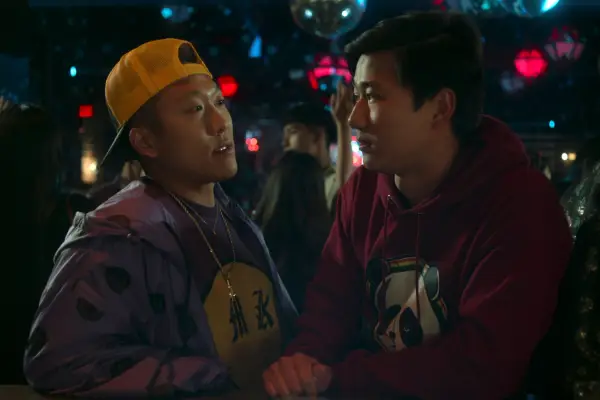 Joon Lee as TK and Sam Song Li as Bruce Sun in The Brothers Sun standing closely together and talking in a nightclub.
