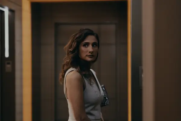 Sarayu Blue as Hilary Star standing in a vest and looking at something.