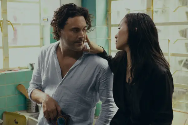 Ji-young Yoo as Mercy touching the cheek of Jack Huston as David, who is leaning in and wearing a blue linen shirt.