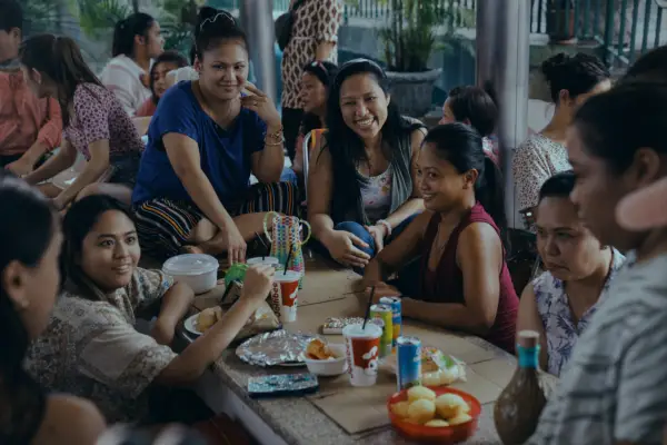 Amelyn Pardenilla as Puri surrounded by women sitting on the floor at a table in the middle of a crowded street