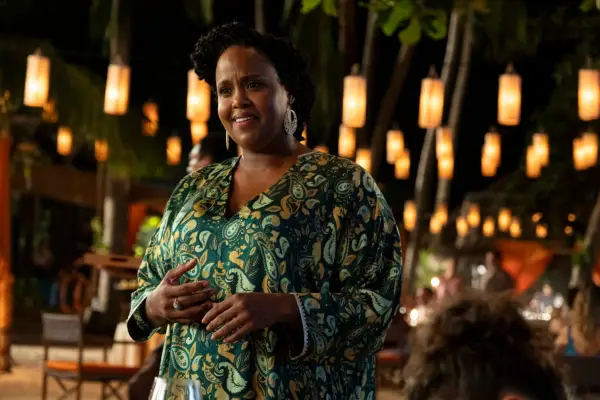 Natasha Rothwell as Belinda Lindsey in a patterned dressed smiling disconcertedly in a candlelit nighttime scene in The White Lotus season 3.