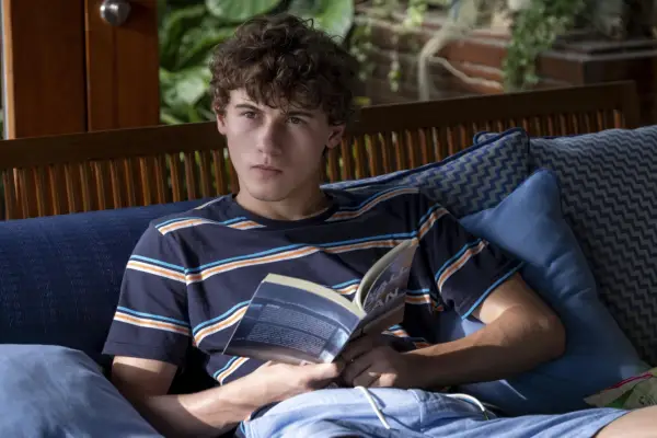 Sam Nivola reclining reading a book but looking up as Lochlan Ratliff in The White Lotus season 3.