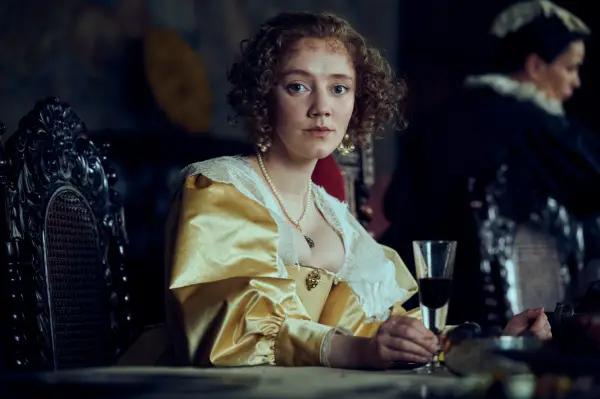 Mirren Mack as Katherine Manners, Duchess of Buckingham in Mary and George at a banquet table with a glass of red wine in Mary and George.