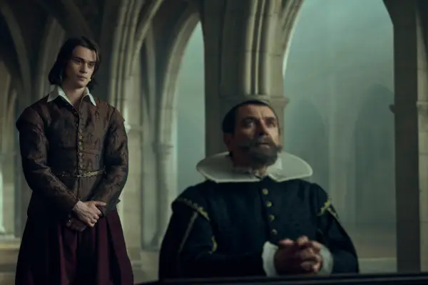Nicholas Galitzine as George Villiers standing behind a bowing Alex Brendemühl as Olivares in Mary and George.