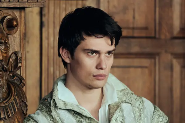 Nicholas Galitzine leaning against a wood panelled wall wearing a white shirt and baroque patterned jacket.