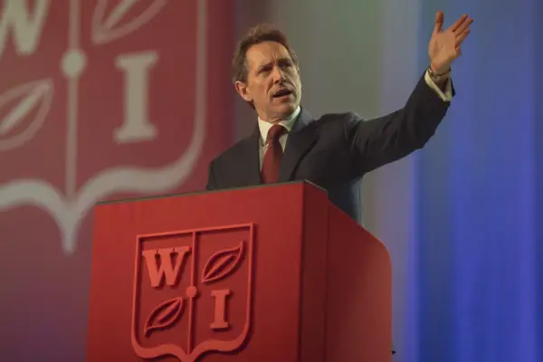 Bertie Carvel as Tony Blair in The Crown standing at a lectern with WI on it