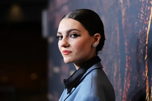 Emily Carey in a light grey suit jacket looking into camera