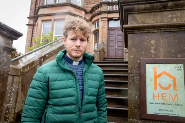 Steven Miller plays Alan Calder, wearing a green jacket, standing at the bottom of some steps outside a homeless shelter