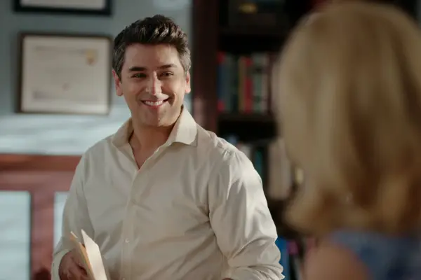Mark Ghanimé as Dr Cameron Hayek, wearing a white shirt and smiling ahead.