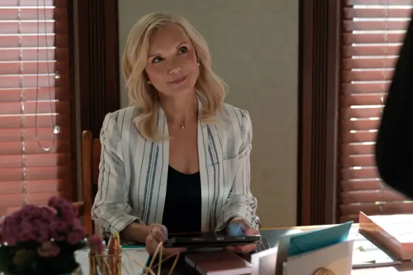 Teryl Rothery as Muriel sat down at a desk, looking up and smiling.