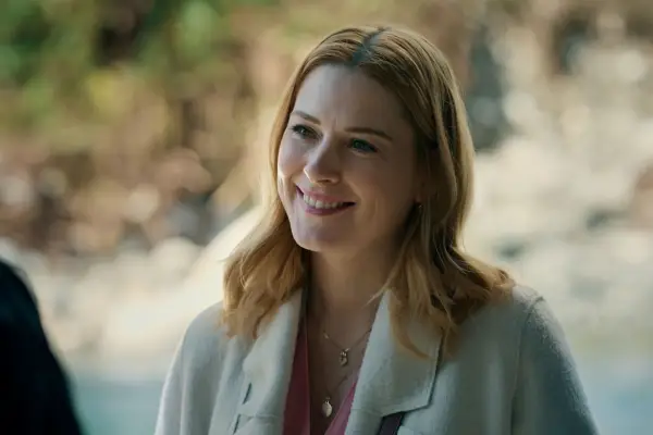 Alexandra Breckenridge as Mel. She is smiling with her head placed to one side, wearing a white jacket and has short strawberry blonde hair.