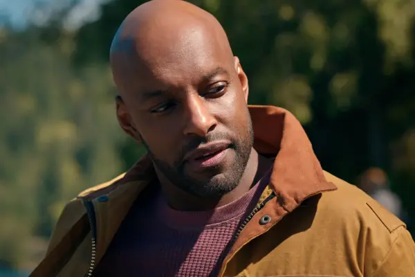 Colin Lawrence as Preacher looking at someone, wearing a purple jumper and brown jacket.