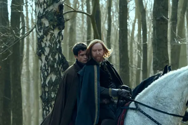 Nicholas Galitzine and Tony Curran riding together on a white horse in the middle of a forest with Nicholas leaning on Tony