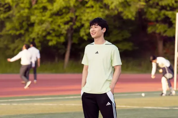 Joshua Lee plays Jin, standing on a sports field with his hands in his pockets, smiling
