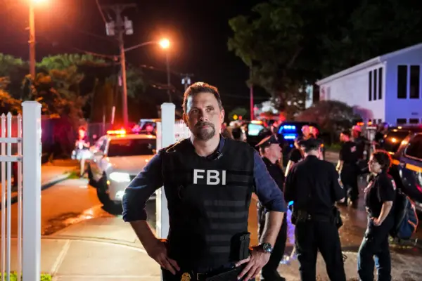 An FBI agent stands with his hands on his hips at a night time crime scene