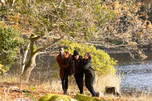 Romario Simpson as Lindo, Melina Akerman Kvie as Elsa Henrik and Hannah Donaldson as Bart in Granite Harbour struggling up a grassy hill by a lake.
