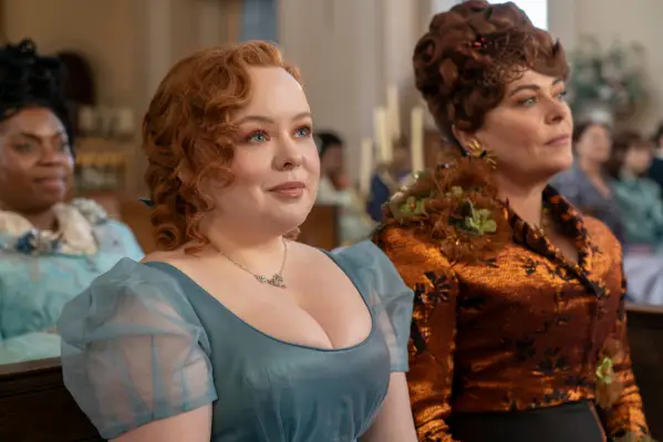 Nicola Coughlan as Penelope Featherington, Polly Walker as Lady Portia Featherington in Bridgerton sitting in formal attire lsmiling