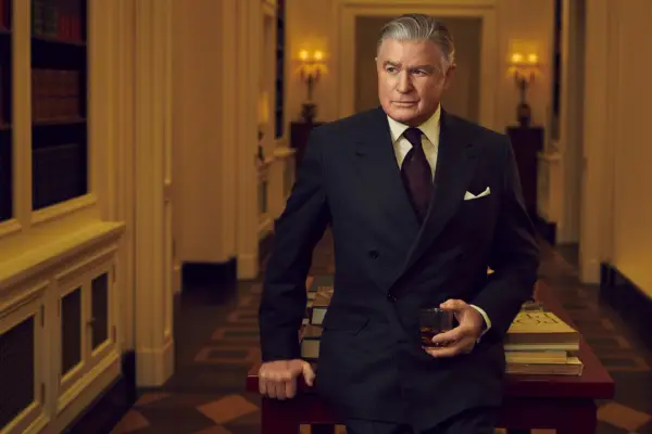 Bill Paley (Treat Williams) wears a smart dark blue suit and stands in his opulent home