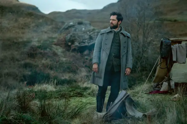 Richard Rankin as Roger Wakefield in Outlander season 7 part 2 standing in the middle of a field and looking lost.