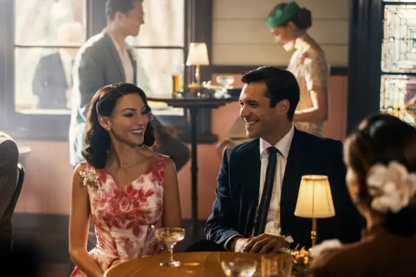 Michelle Keegan as Kate and Nic English as Robbie in Ten Pound Poms season 2 sitting down in a bar and laughing.