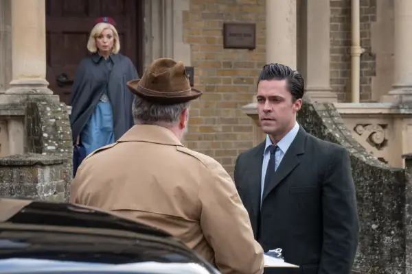 Olly Rix speaking to a gentleman in a brown jacket and hat while Helen George looks over