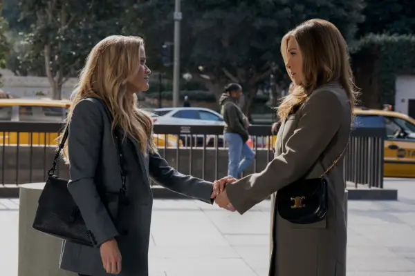 Reese Witherspoon and Jennifer Aniston as Bradley and Alex in The Morning Show, holding hands on a pavement.