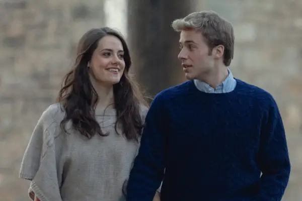 Ed McVey as Prince William and Meg Bellamy as Kate Middleton in The Crown, walking together and holding hands